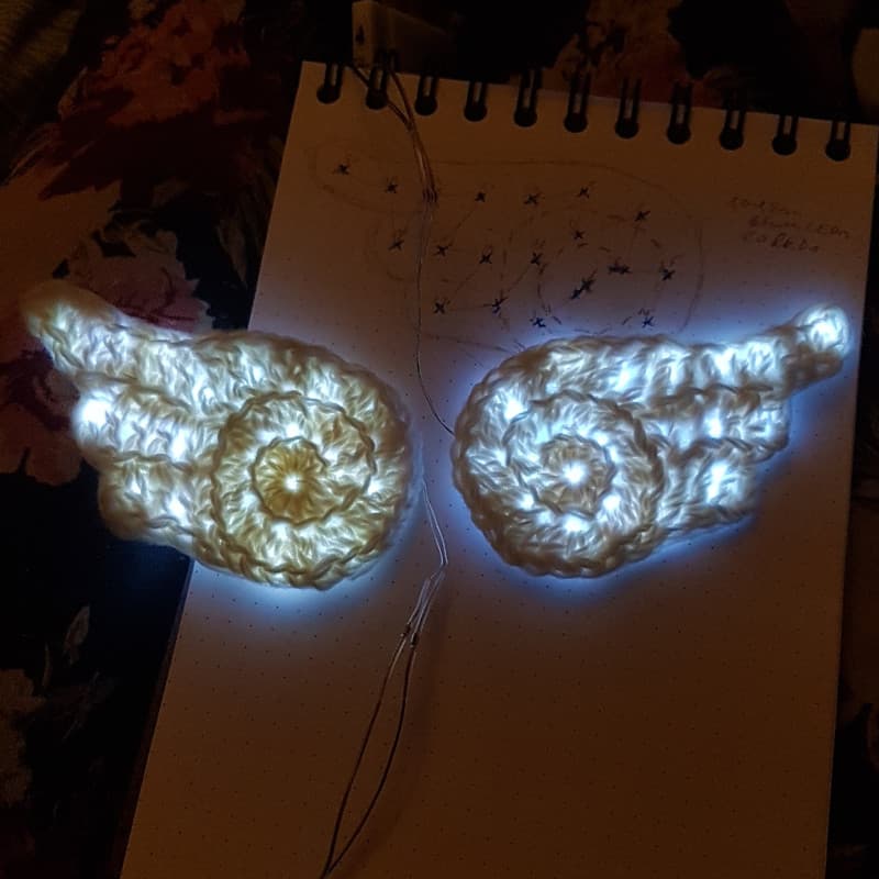 the two lit-up crochet wings side by side, with the LED placement sketch seen underneath