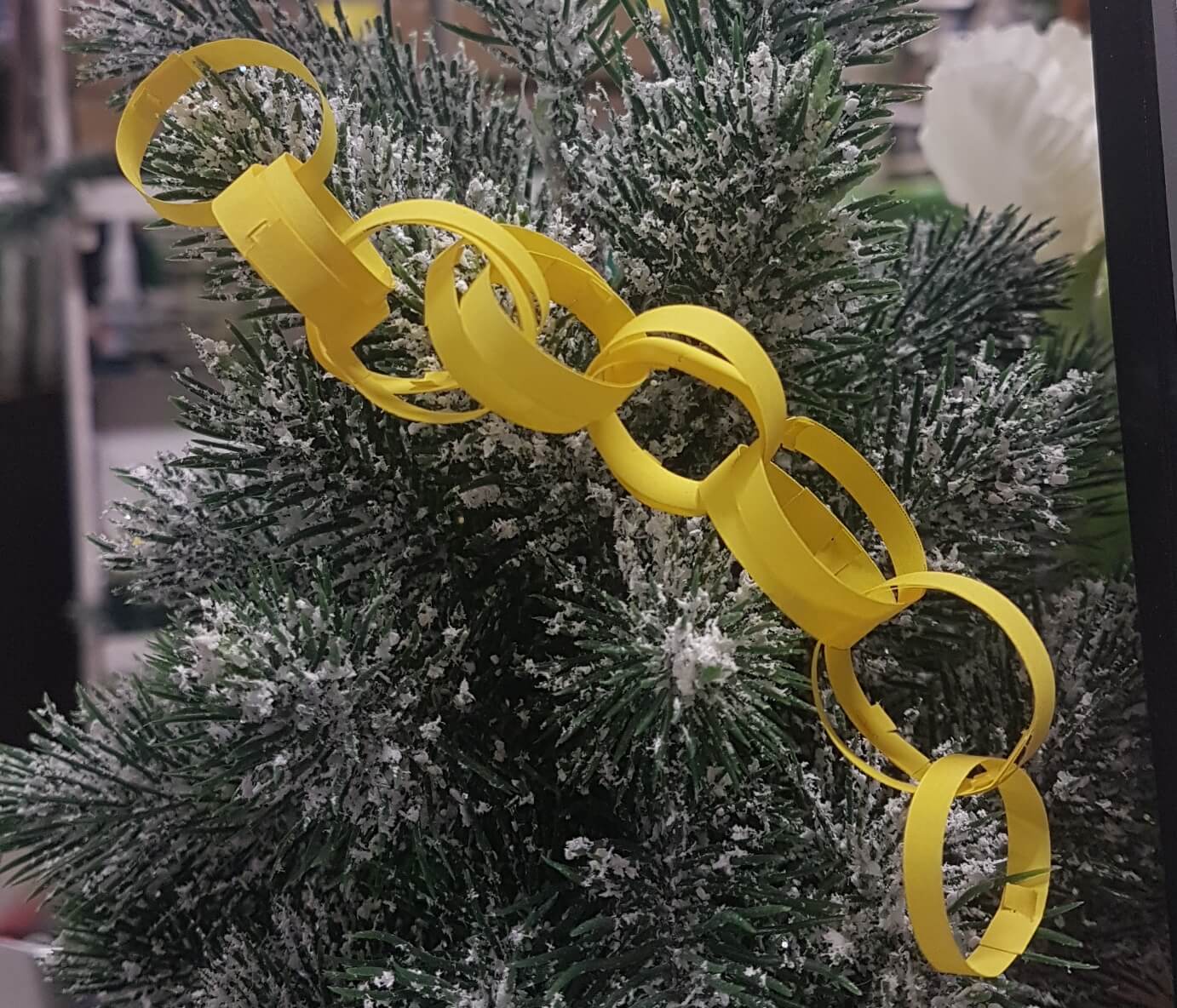a tiny yellow paper chain, with doubled links, draped on a tiny fake snowy tree