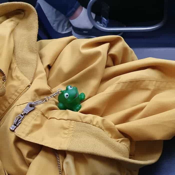 frog keychain atop yellow jacket bunched on a plane seat