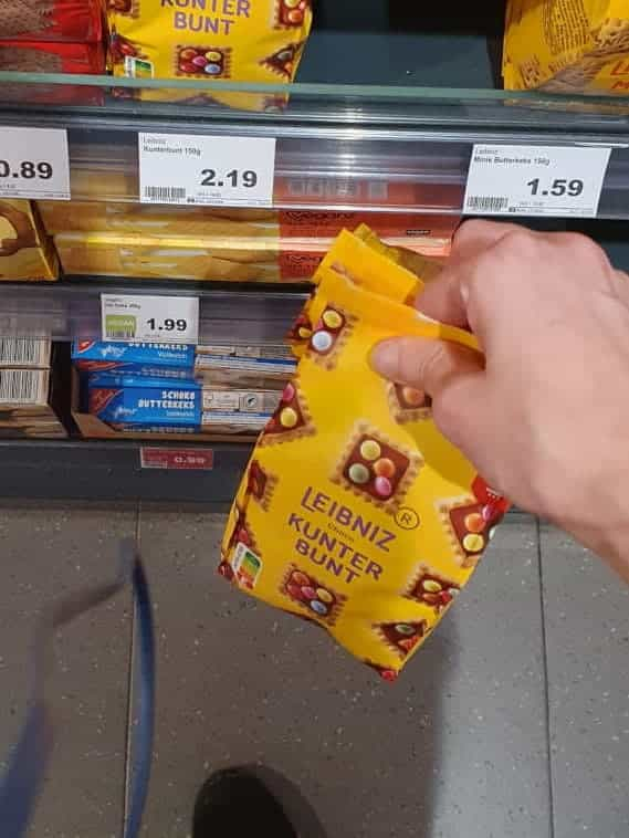 me holding two packs of leibniz kunterbunt cookies (squares with chocolate covering and sugar-coated dragées atop) at a grocery store