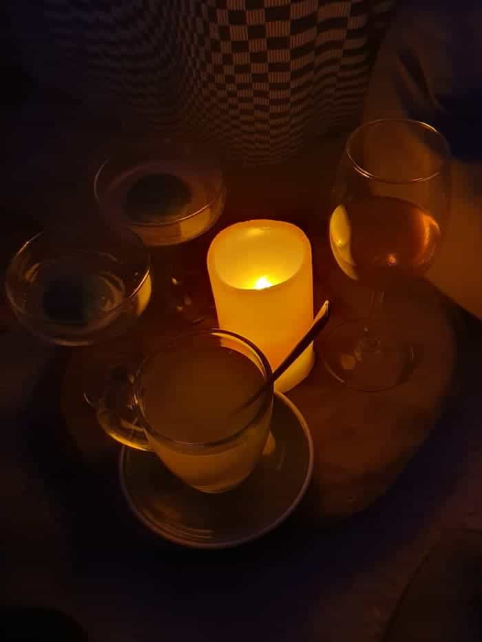 a glass mug of tea, two cocktail glasses and a wine glass snug around a fake candle on a wooden block on the floor