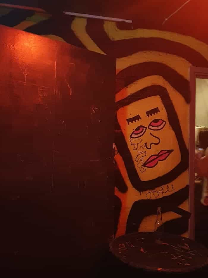 eye-rolling cartoonish face painted within black squiggly lines on a yellow wall, in a corridor