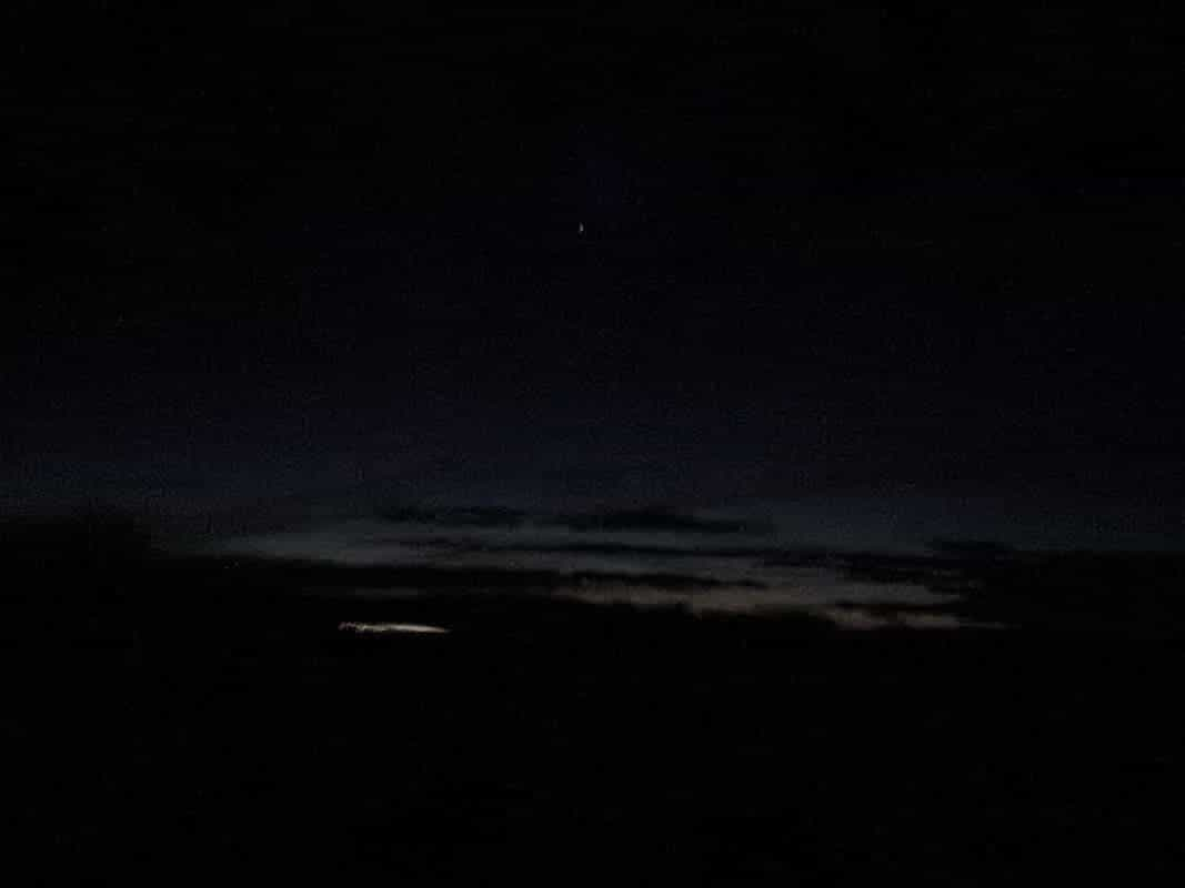 late dusk, with some clouds peppering a barely lit and gradiented sunset sky, seen from a bus window