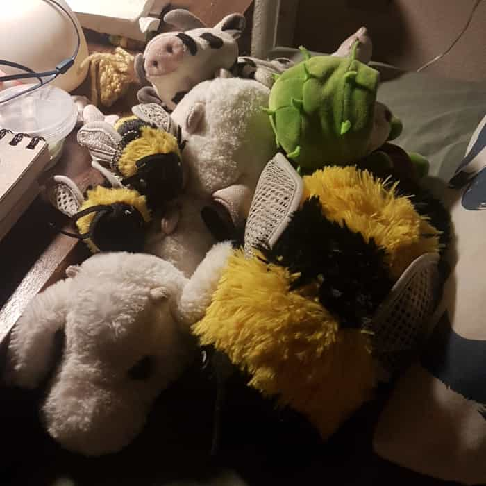 various plushies at bedside: a dragon, 1 big and 2 tiny bees, a chestnut teddy bear, a cow