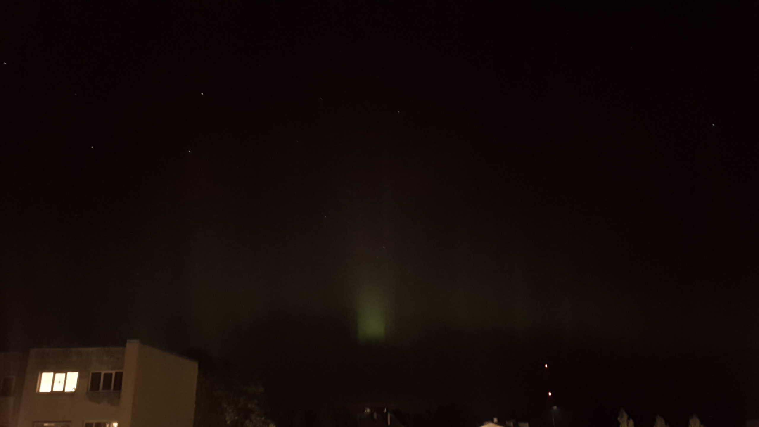 the northern lights as seen from my window, in faint green at the bottom and fainter purple at the top, with faint columns to it