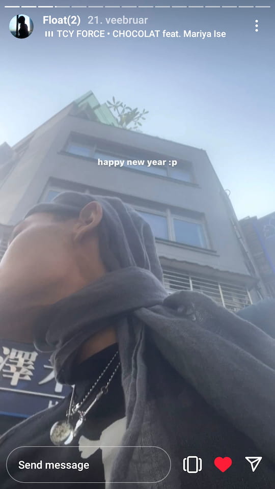 oli xl instagram story pic - selfie taken at lower angle as he stands in front of some building, he looks away to the side, head and neck lightly wrapped in a scarf, very attractive; inserted text says 'happy new year :p'