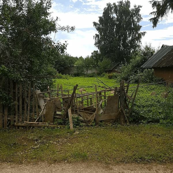 a fence in the outskirts mended in the most raggedy way with planks, branches, etc