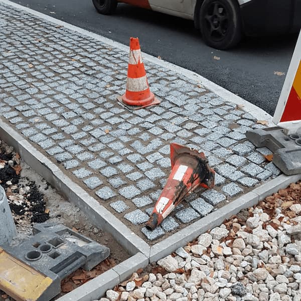 mid-renovation sidewalk with two traffic cones, one smeared and on its side, and a clean one stood further away
