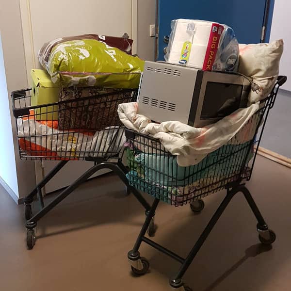 two shopping carts loaded with blankets, a microwave, other stuff, in a dorm apartment lobby