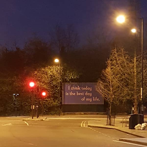 small blue billboard saying 'I think today is the best day of my life.' at an intersection