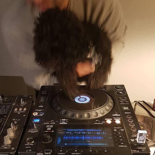 a midsize black poodle being held, with its paws atop a CDJ to feign record scratching