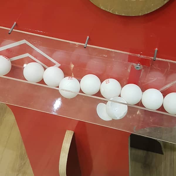 table tennis balls, one of them broken open, in a plastic container attached to a stand