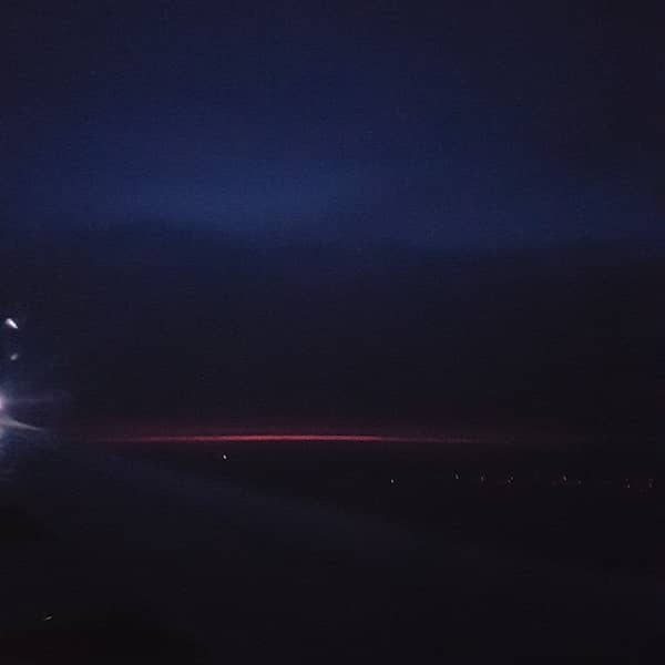 very small strip of reddish sunset glow from below a layer of cloud, shot from a plane upon descent