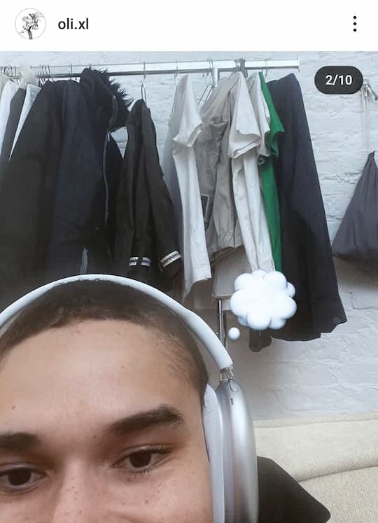 2nd pic of oli's post: closeup of top half of his face, with freckles, as he's sat in front of a clothes rack, headphones on