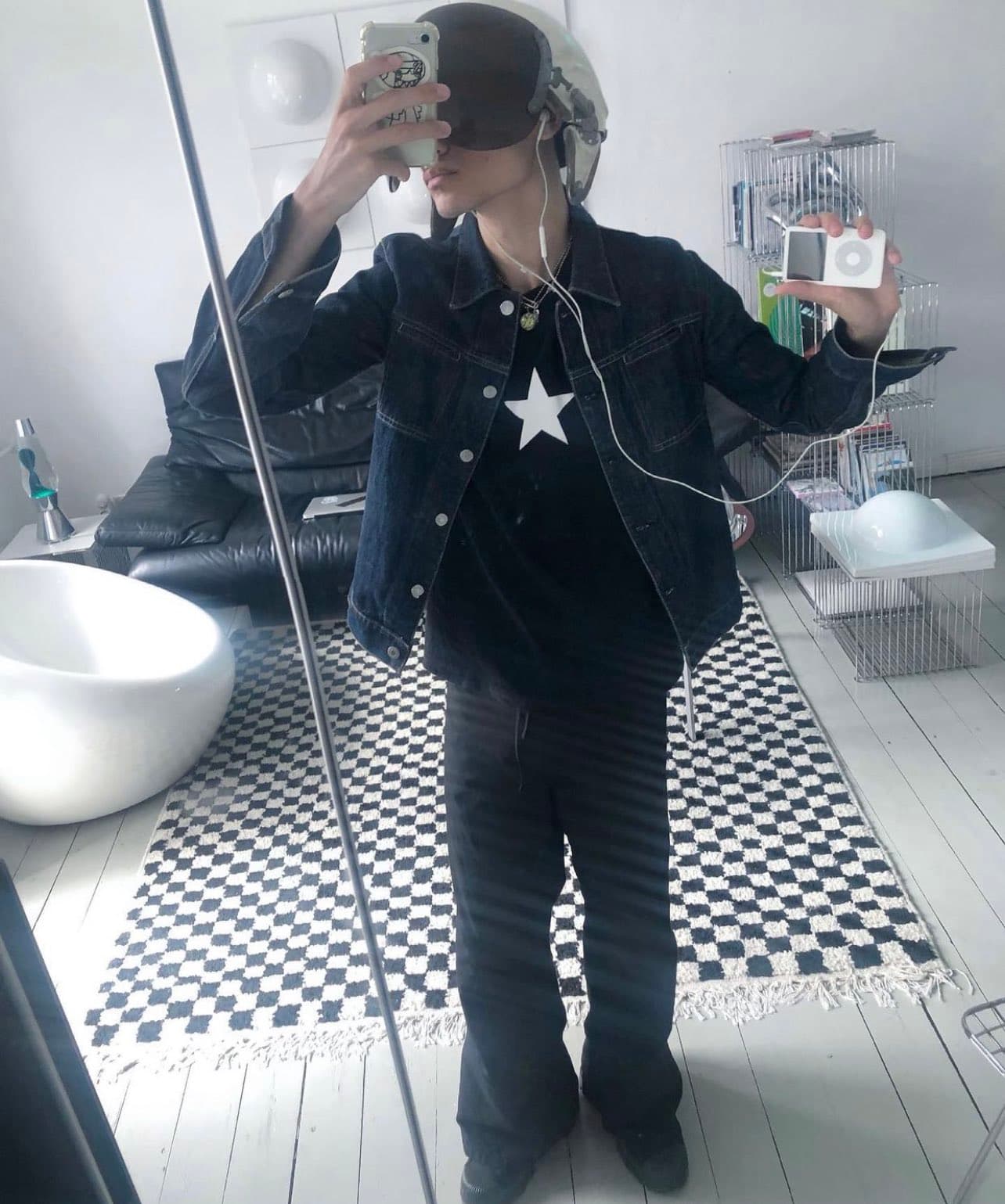 oli (lighter-skinned, thin, androgynous-looking) posing for a mirror selfie, wearing a soviet pilot helmet and a dark-colour fit, and holding an ipod with wired earbuds